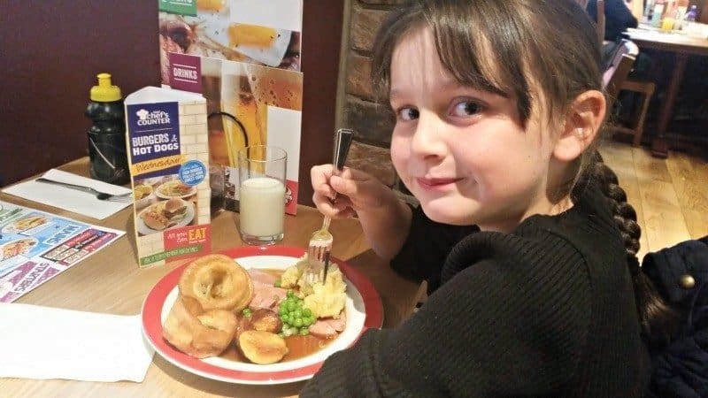 A young boy sitting at a table with a plate of food, with Brewers Fayre and Value menu