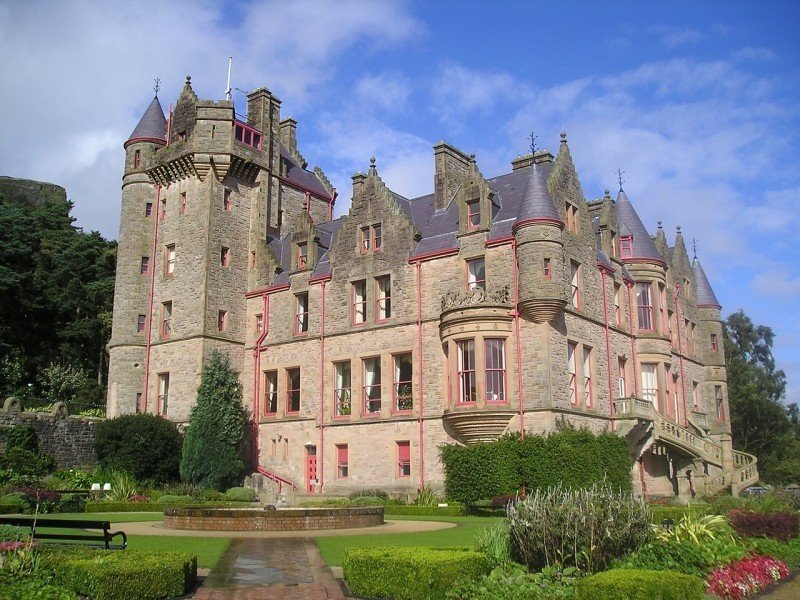 A castle with a clock tower in front of a house with Belfast Castle in the background