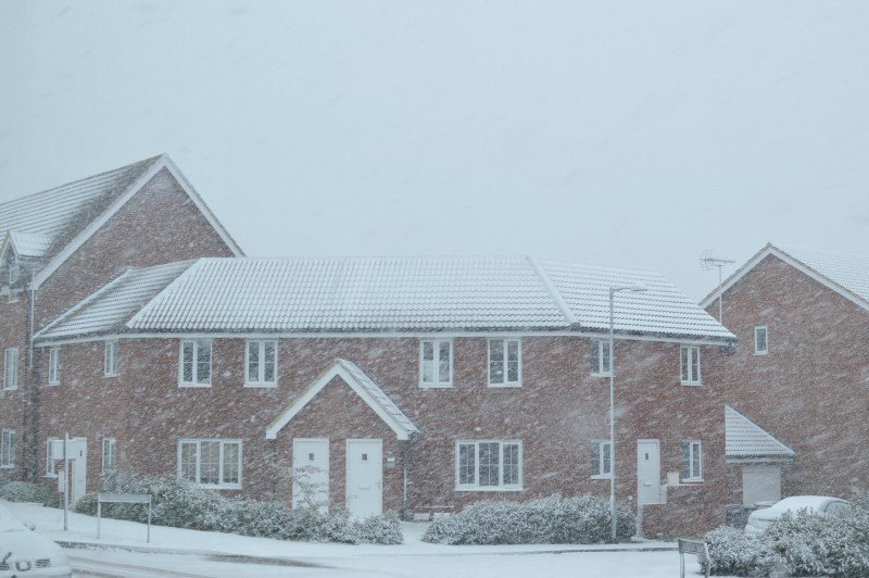 A house covered in snow in front of a brick building