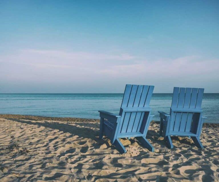 A couple of lawn chairs sitting on top of a sandy beach