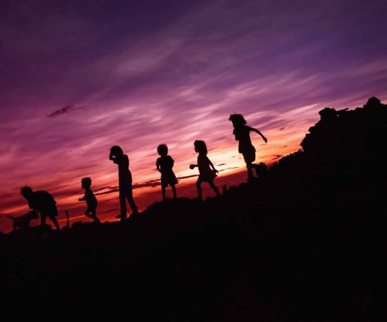 A group of people walking up a hill with a sunset in the background