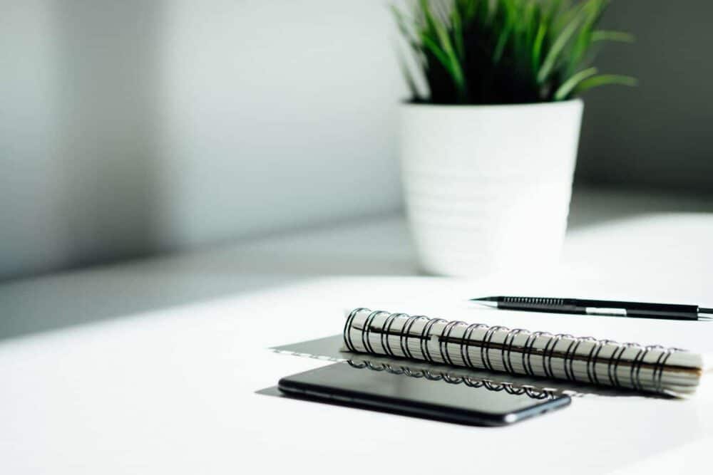 Start Your own Blog - pen, notebook, and smartphone on a white table with plant