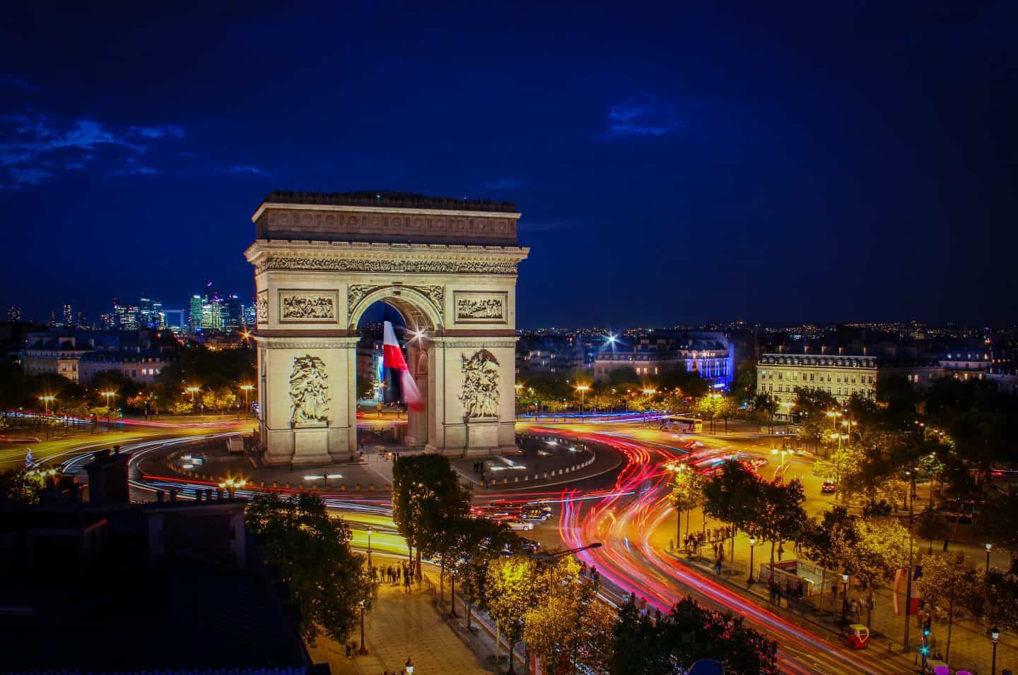 A large clock tower towering over Arc de Triomphe at night