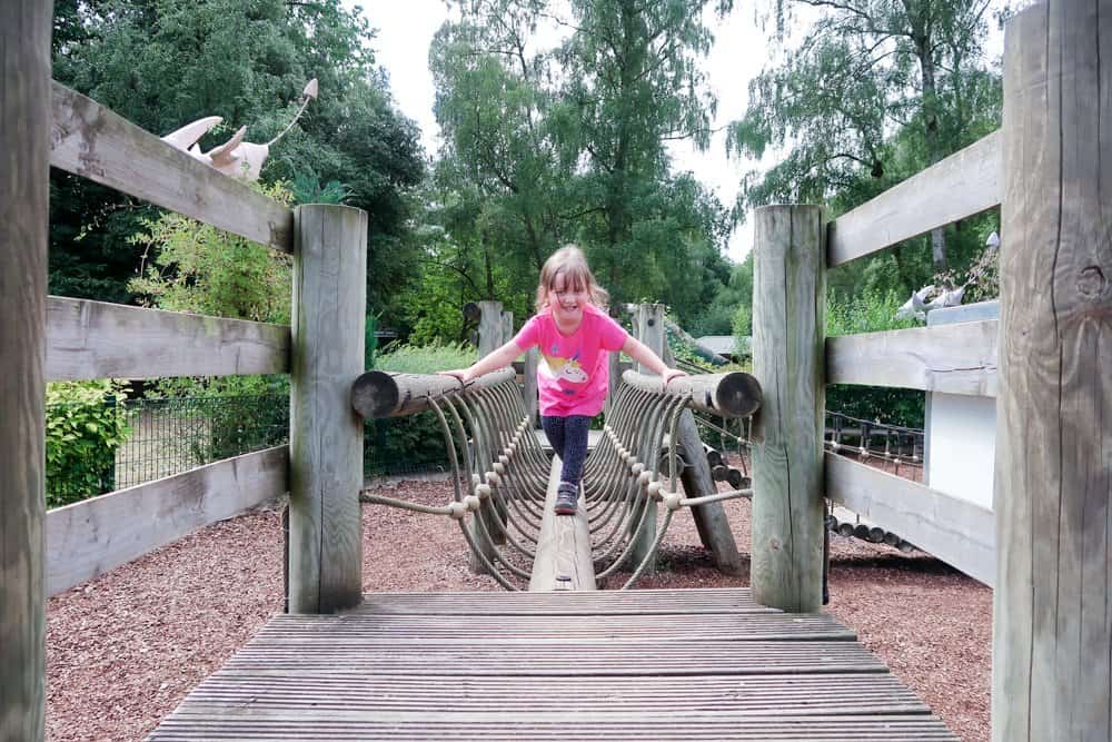 A visit to ROARR! Dinosaur Adventure - child in a pink Frugi top playing on a wooden climbing frame