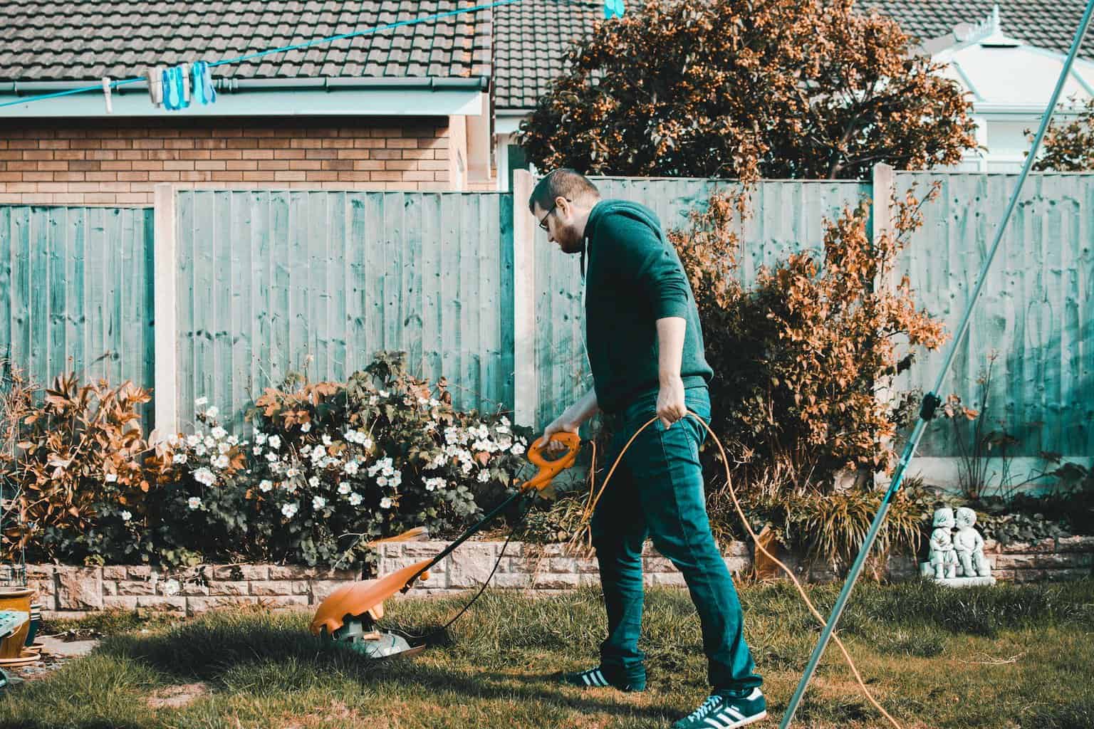 man holding orange electric grass cutter on lawn - random acts of kindness you can do as a family