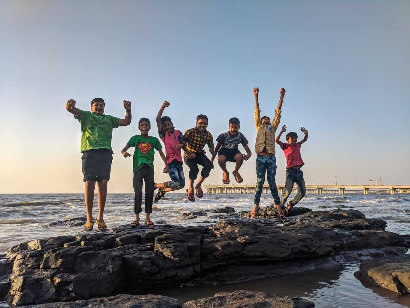 boy wearing green crew neck shirt jumping from black stone on the seashore - Common Struggles of Raising a Teenager to Be Aware Of