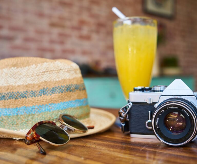 gray and black dslr camera beside sun hat and sunglasses