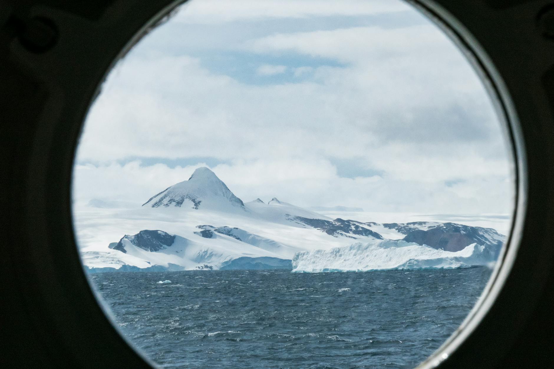 a snow covered mountain beside the sea with a view from a porthole