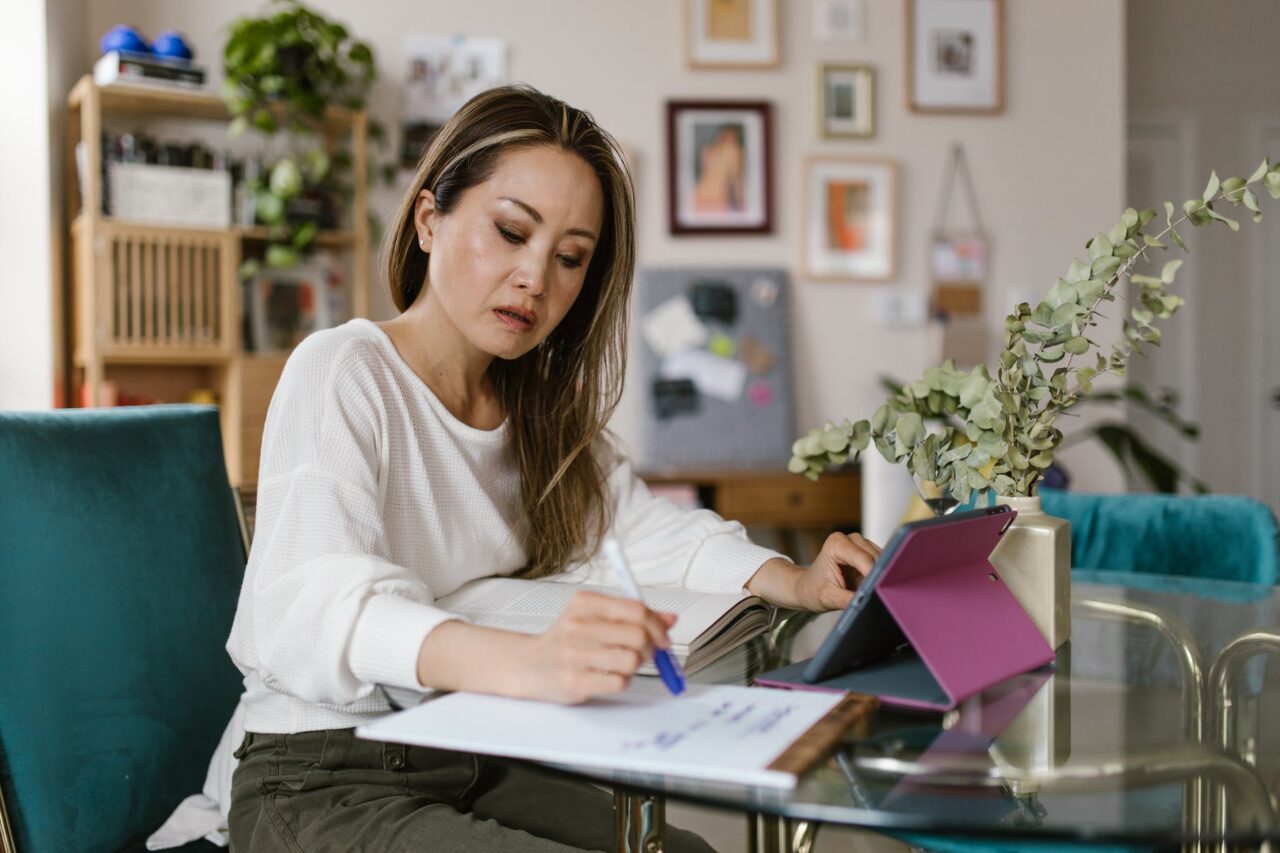 woman using a tablet computer while writing on paper